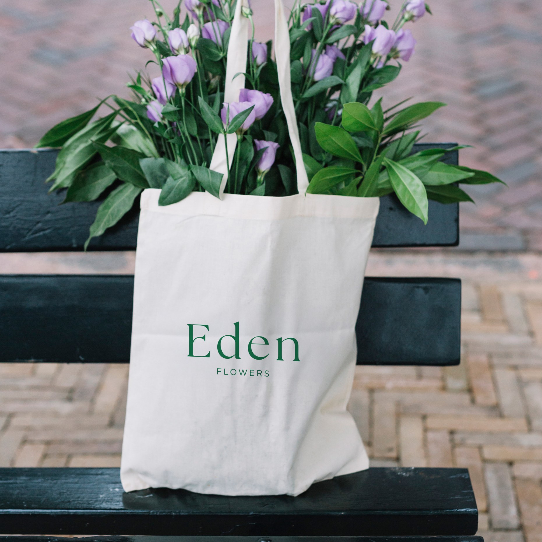 Canvas Eden tote bag on a bench, filled with lilac lisianthus